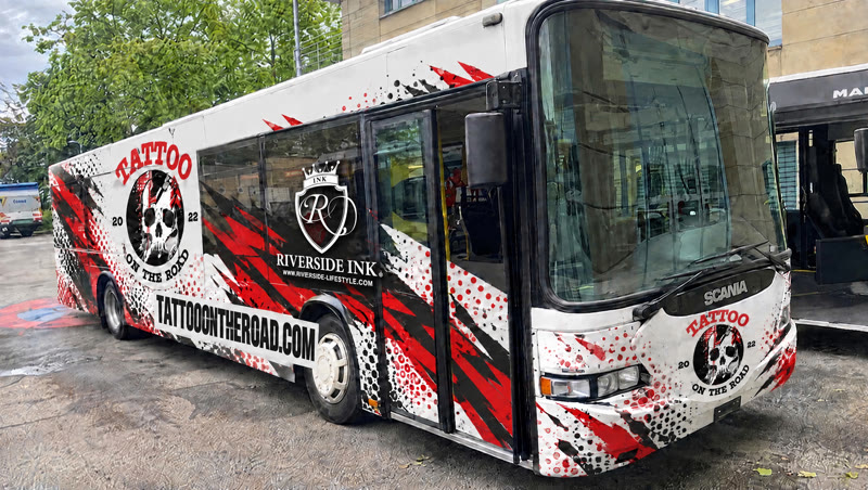 Der Tattoo-Bus, ein Scania-Stadtbus im Totenkopf-Design mit Totenkopf-Logo, rot-schwarzen Splittern, Riverside-Ink-Wappen mit www.riverside-lifestyle.com und dem Schriftzug tattooontheroad.com.